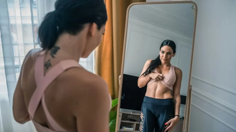 Woman in workout clothes checking her abs in the mirror, focusing on body image and self-reflection